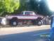1989 Ford Bronco - A lifted red and white pickup truck with large tires is parked on the side of the road next to another vehicle.