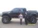 1989 Ford Bronco - A heavily modified black Ford Super Duty pickup truck is shown with two people posing beside it.