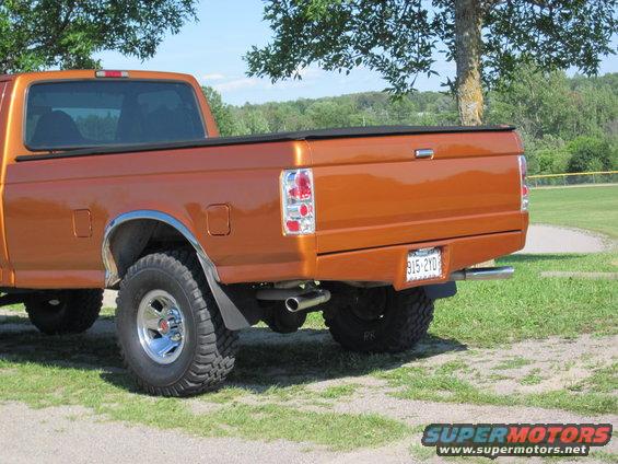 Orange pickup truck rear view, showing tailgate, taillights, and chrome wheels