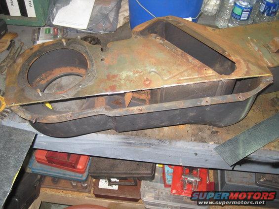 Old, rusty metal housing for a vehicle's heater core, sitting on a workbench with tools and storage bins nearby