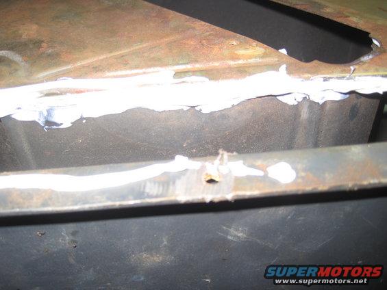 Close-up of rusted metal panel with white sealant applied, showing a small hole