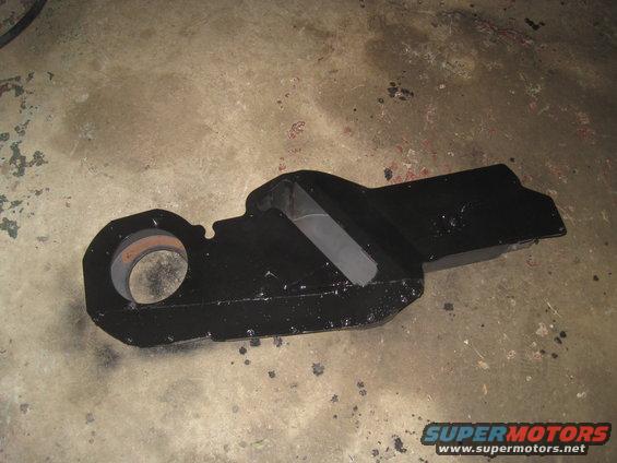 Black metal automotive part with a circular opening on one end, resting on a concrete floor