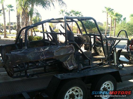 Burnt-out vehicle frame on a trailer, showing roll cage and damaged body panels
