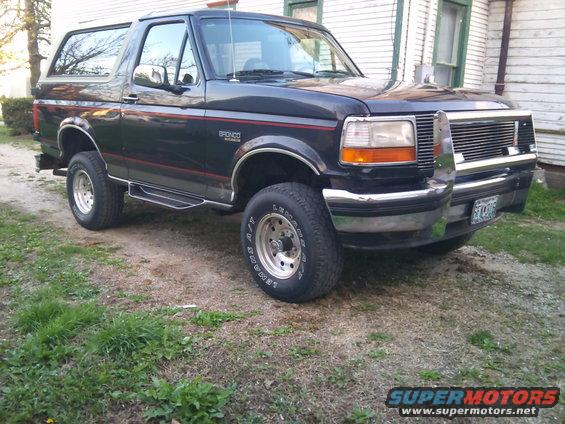 1994 Ford Bronco parked on a dirt lot next to a house