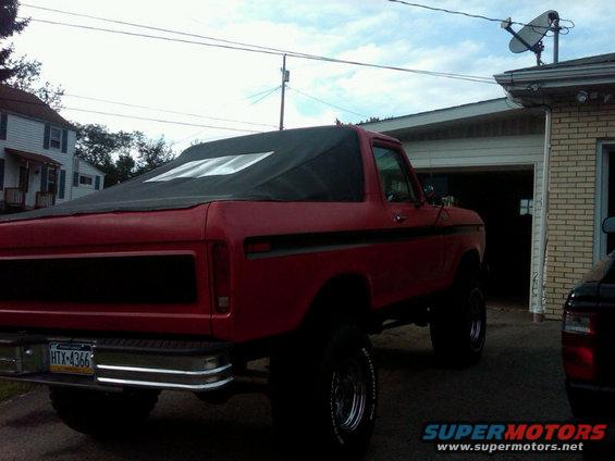 Red 1978 Ford Bronco with black soft top, rear 3/4 view, lifted suspension, chrome bumper, license plate HTX-4366