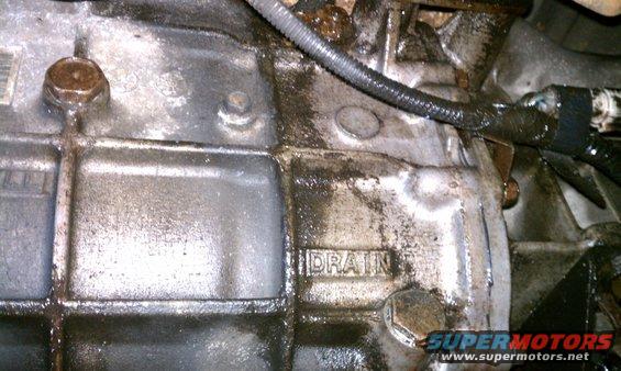 Close-up of a greasy transmission casing with the word DRAIN visible