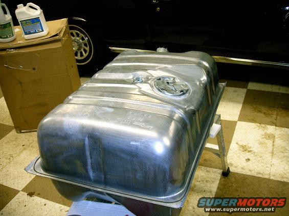 Metal fuel tank on a stand, with a black vehicle and cardboard box in the background