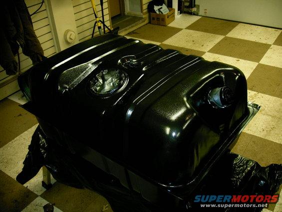 Black fuel tank with two circular openings on top, sitting on a stand covered in plastic