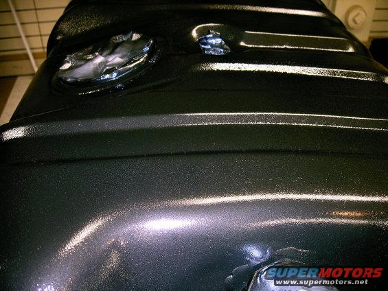 Black metal fuel tank with two circular openings and textured surface