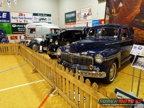 Dark blue 1948 sedan with chrome grille and headlights, parked behind a wooden fence