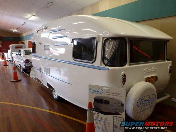 White caravan with blue trim and a spare tire cover, parked next to a white pickup truck