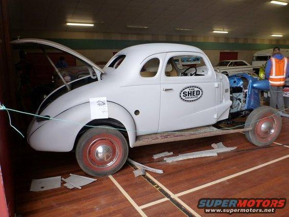 White hot rod coupe with hood open, showing unfinished interior and exposed engine bay. "The Shed" logo on door
