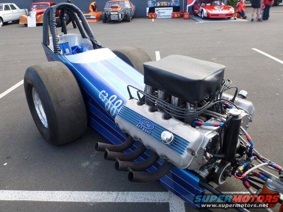 Blue dragster with white stripes, large rear tires, and a Ford 327 SOHC engine. Visible text includes 'Ford' and 'SUPERMOTORS'