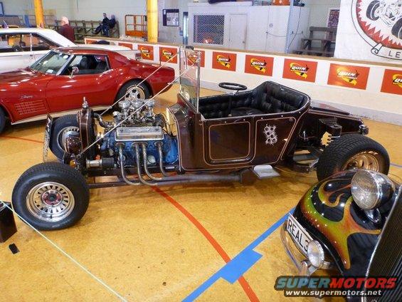 Hot rod with exposed V8 engine, dark brown body, and custom flames on front fender