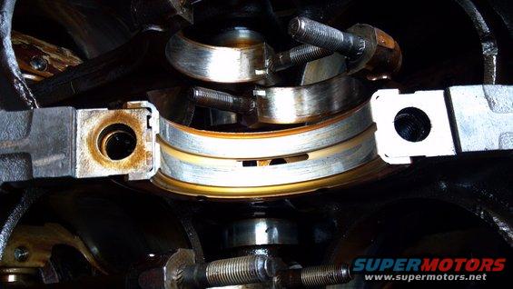 Engine crankshaft bearings with visible wear and oil residue. Part of a Supermotors.net engine rebuild