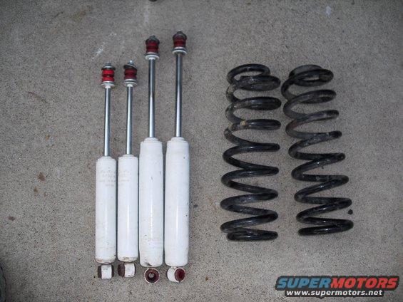 Four white shock absorbers and two black coil springs on a concrete surface