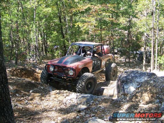 Off-road buggy with big tires navigating a rocky trail, another vehicle visible in the background