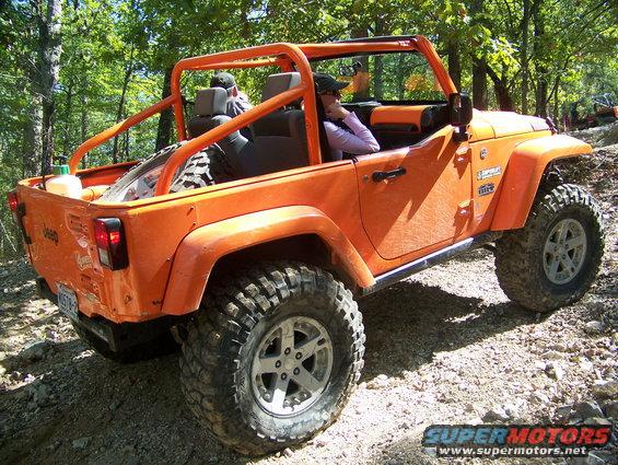 Orange Jeep Wrangler with roll cage, spare tire in back, on a dirt trail