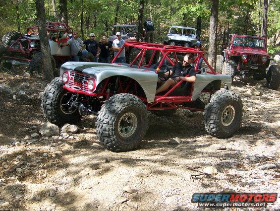 Custom buggy with red roll cage and big tires, other off-road vehicles in background