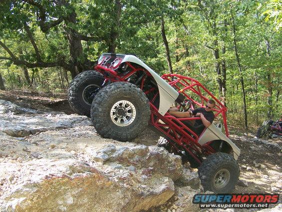 Off-road buggy with red roll cage and large tires climbing rocky terrain