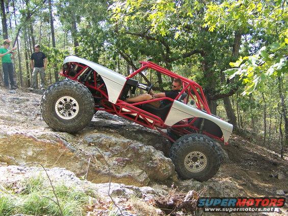 Custom buggy with red roll cage climbing rocks on a wooded trail