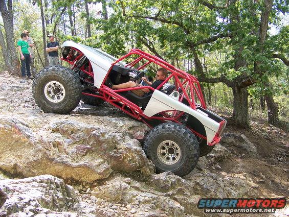 Buggy with red roll cage climbing over rocks on a trail