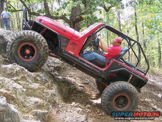 Red Jeep off-roading, climbing a rocky incline with a roll cage