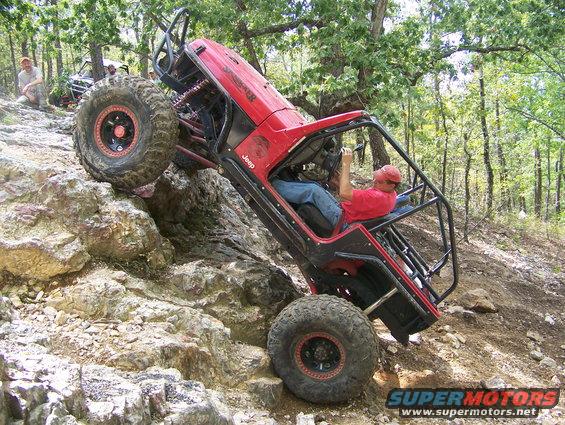 Red Jeep off-roading on a rocky incline, another vehicle visible behind