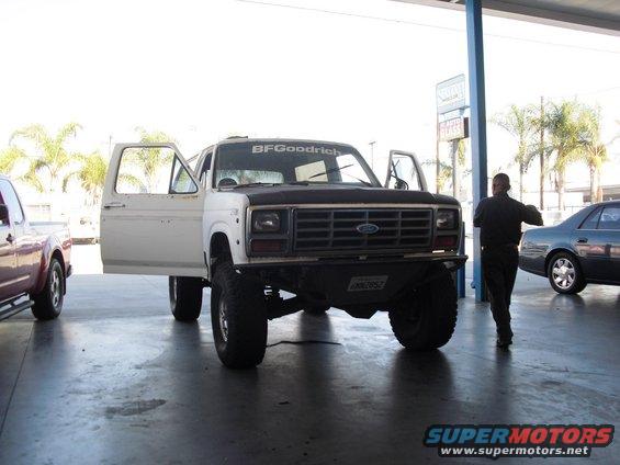 White Ford Bronco with doors open, BFGoodrich sticker on windshield. Another vehicle to the left, car to the right