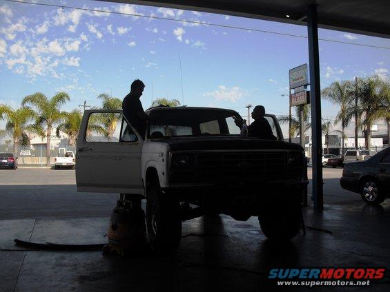 1986 Ford Bronco with doors open, two people working on it inside a garage