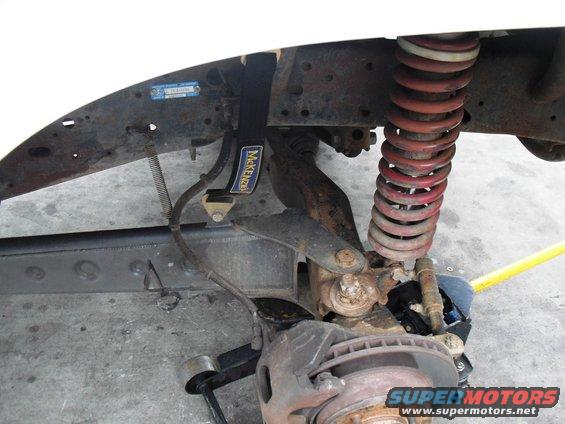 Vehicle suspension with red coil spring, rusty brake rotor, and a black strap labeled "McKenzie"