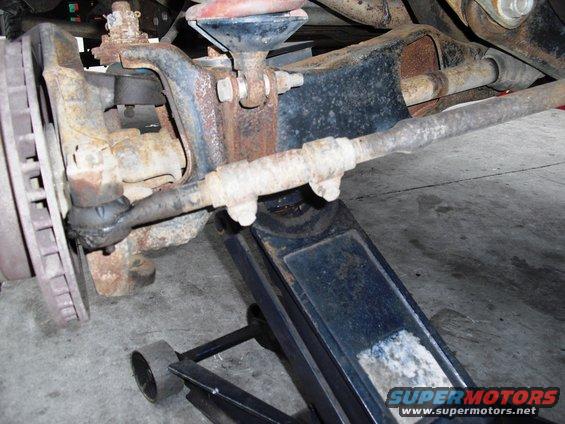 Rusty vehicle steering linkage and suspension parts supported by a floor jack