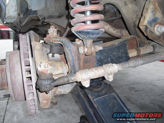Rusty vehicle suspension with coil spring and brake rotor, supported by a jack