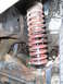 1986 Ford Bronco - Close-up view of a front suspension shock absorber and red coil spring assembly.