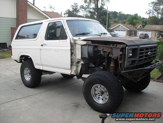 White Ford Bronco with hood removed, showing engine bay. Front fender is missing