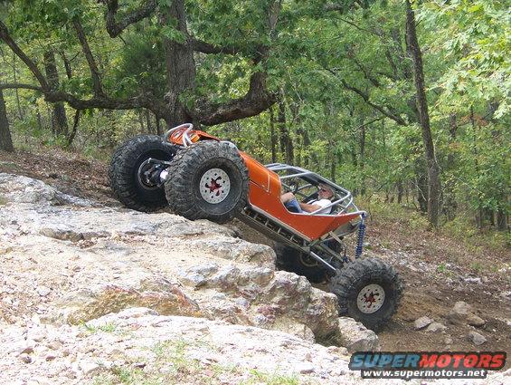 Custom orange off-road buggy with large tires climbing a rocky incline
