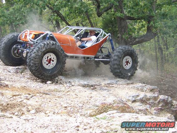 Orange buggy with large tires driving over rocks on a dirt trail