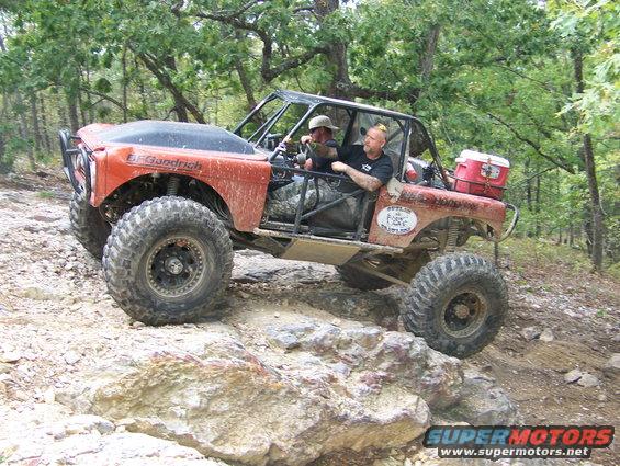Red off-road vehicle with BFGoodrich tires on rocky terrain, two people inside