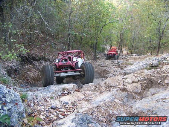 Two custom off-road buggies navigating a rocky, wooded trail
