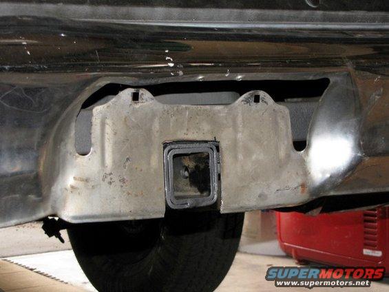 trailer hitch receiver mounted under a vehicle bumper, with a tire visible below