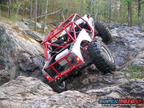 Off-road vehicle with red roll cage climbing rocks