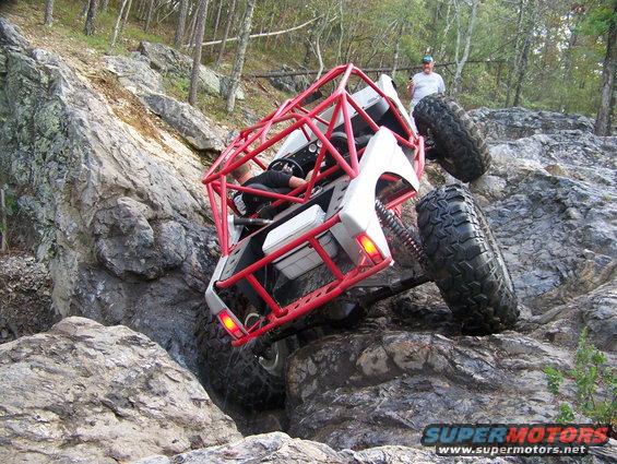 Off-road buggy with red roll cage climbing over large rocks on a trail