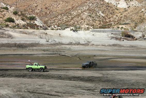 Green pickup truck and black SUV off-roading in a dry, dusty area