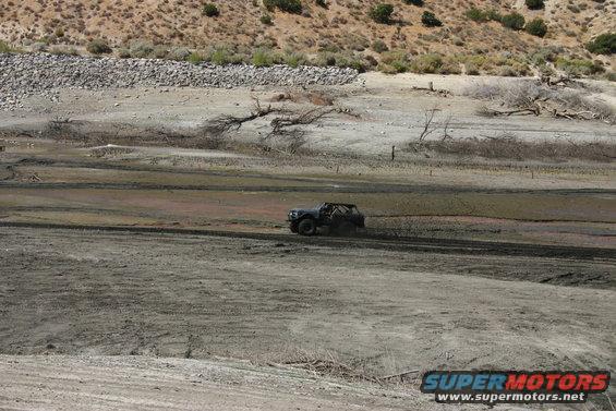 Off-road vehicle driving through a muddy, dry lakebed with hills in the background