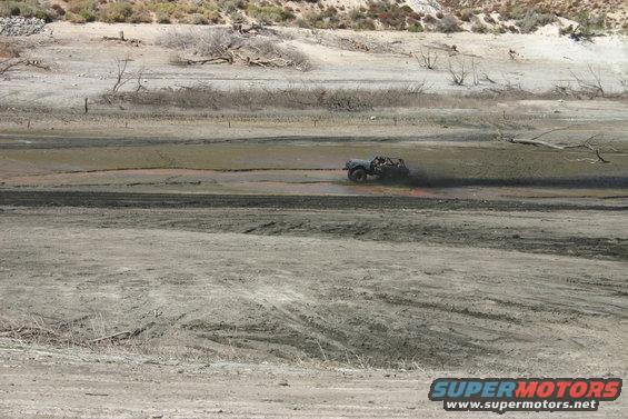 Jeep-like vehicle kicking up mud while driving through a dry lake bed