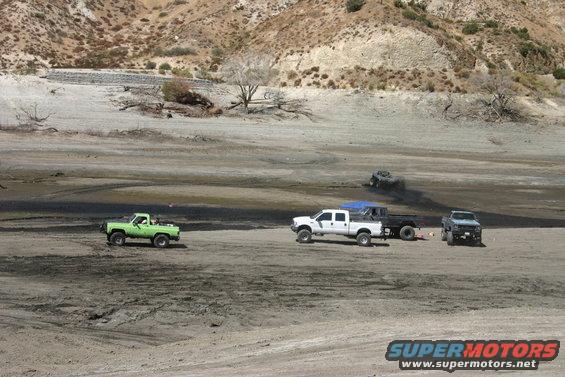Green pickup truck driving in a dry lake bed with other vehicles