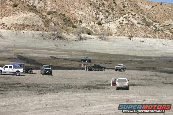 Several trucks and SUVs parked in a dry, dusty landscape with hills in the background