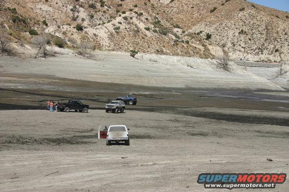 several trucks and SUVs parked in a dry, dusty area with hills in the background