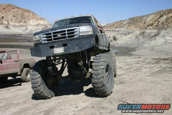 Black lifted Ford F-Series truck with large tires and custom bumper, parked next to a red Jeep