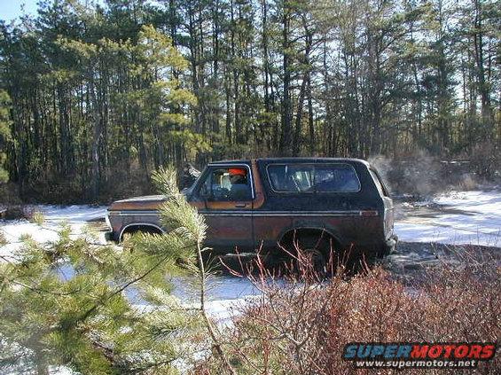 Side view of a rusty 1978 Ford Bronco in a snowy, wooded area